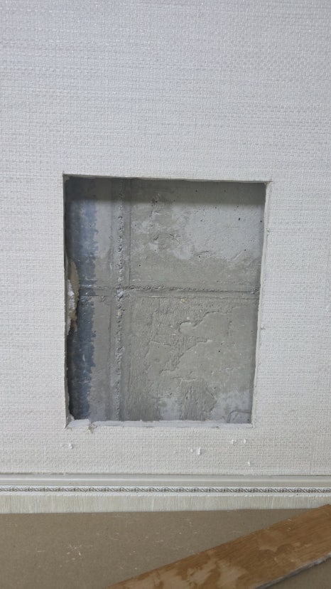 Concrete wall and adhesive dabs exposed behind drywall